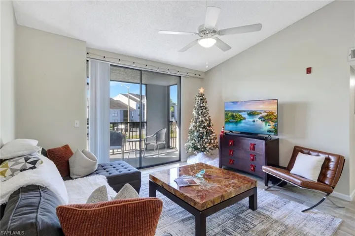 Living room with light wood-style tile floors, vaulted ceiling, and ceiling fan
