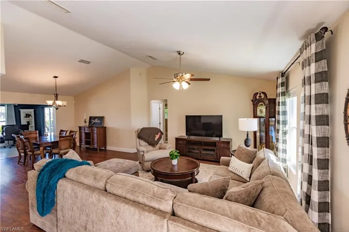 Living room featuring ceiling fan with notable chandelier, dark hardwood / wood-style floors, and lofted ceiling