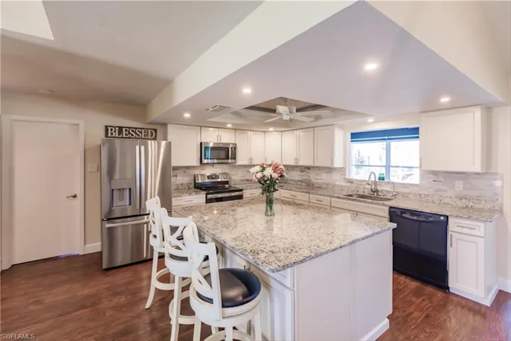 Kitchen with stainless steel appliances, sink, white cabinetry, dark hardwood / wood-style floors, and a kitchen island