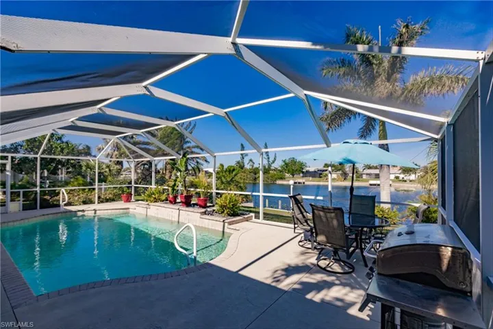 View of pool featuring glass enclosure, a patio area, a water view, and area for grilling