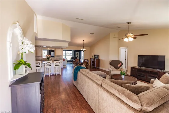 Living room with high vaulted ceiling, dark wood-type flooring, and ceiling fan with notable chandelier