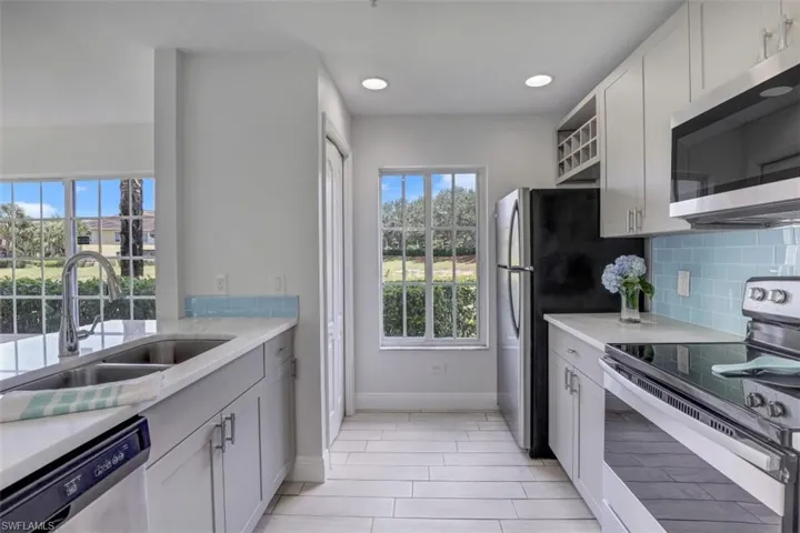 Kitchen featuring a sink, tasteful backsplash, stainless steel appliances, baseboards, and white cabinets