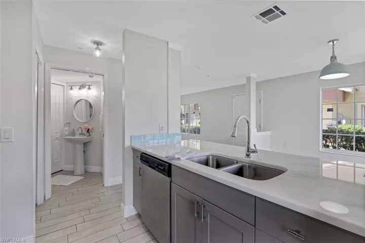 Kitchen featuring a wealth of natural light, gray cabinets, a sink, stainless steel dishwasher, and visible vents