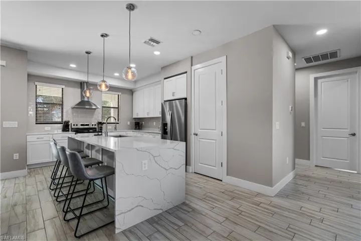 Kitchen with white cabinets, light stone countertops, a kitchen bar, pendant lighting, and wood finish floors