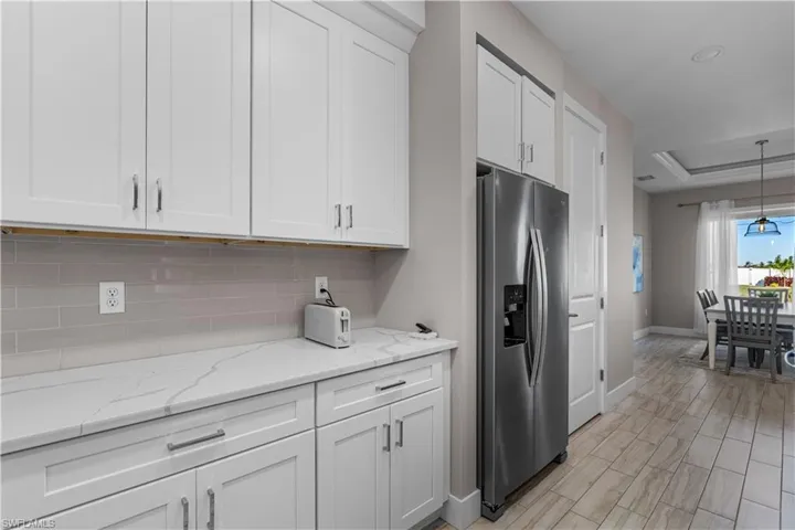 Kitchen featuring stainless steel fridge with ice dispenser, white cabinets, light stone counters, pendant lighting, and a tray ceiling