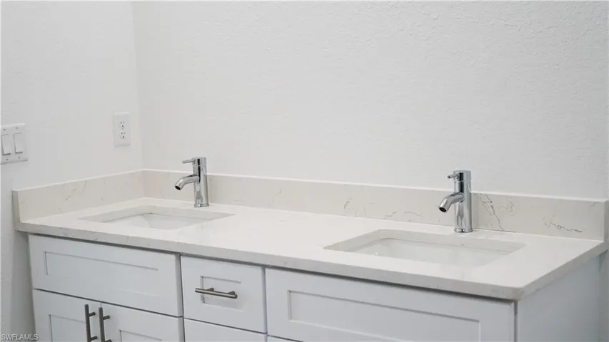 Dual vanity with white shaker-style cabinetry, chrome hardware, and undermount sinks set in a light-toned countertop with integrated backsplash
