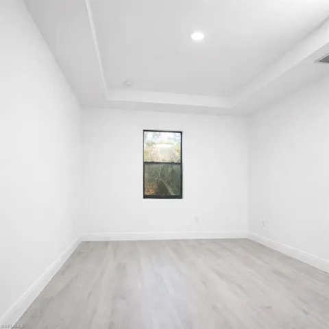 Interior room featuring light wood-finish flooring, white walls, and a single window with dark trim