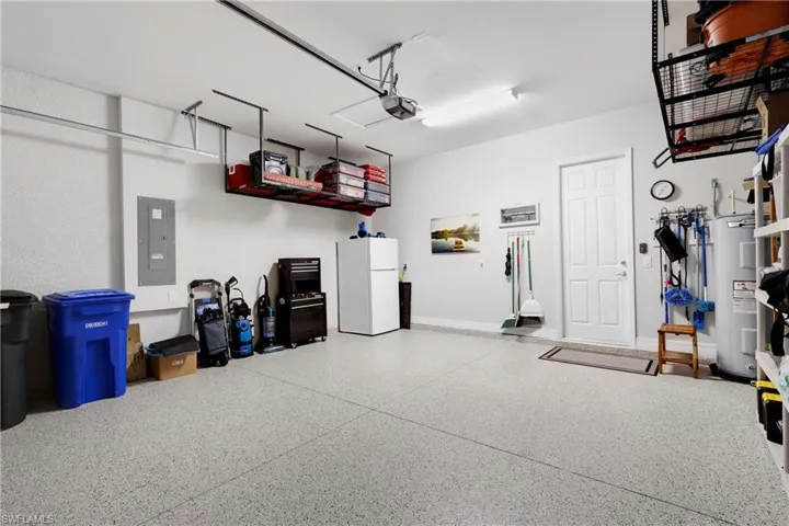 Garage with a garage door opener, electric panel, water heater, and white refrigerator