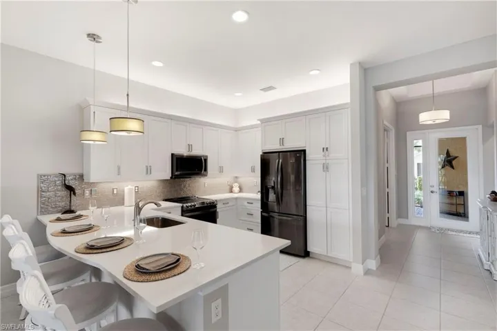 Kitchen with hanging light fixtures, range with electric stovetop, kitchen peninsula, and black refrigerator with ice dispenser