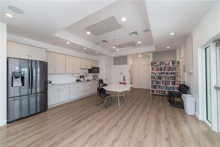 Kitchen with stainless steel fridge, a tray ceiling, light countertops, light wood-style flooring, and recessed lighting