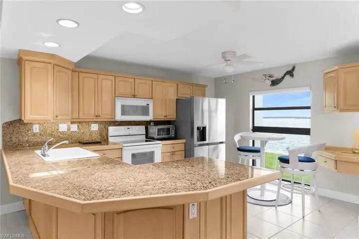 Kitchen featuring light tile patterned flooring, light brown cabinetry, white appliances, a peninsula, and recessed lighting