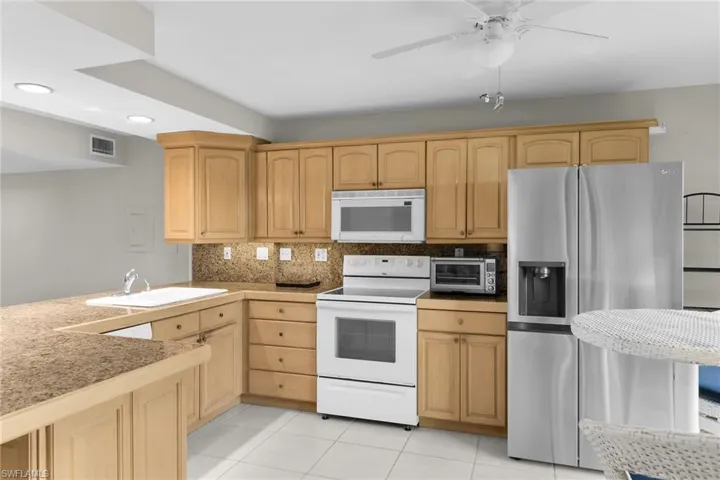 Kitchen featuring white appliances, tasteful backsplash, light brown cabinetry, light tile patterned flooring, and a ceiling fan