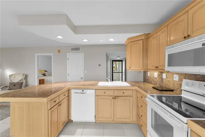 Kitchen featuring white appliances, tile counters, light brown cabinets, recessed lighting, and a peninsula