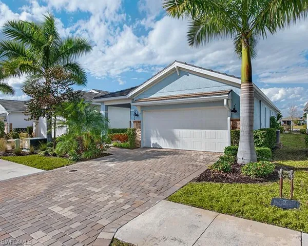 Welcoming front exterior with tropical landscaping and a paver driveway plus the two-car garage.