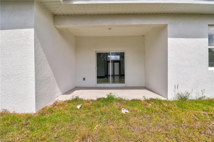 View of exterior entry with stucco siding, a patio, and a lawn
