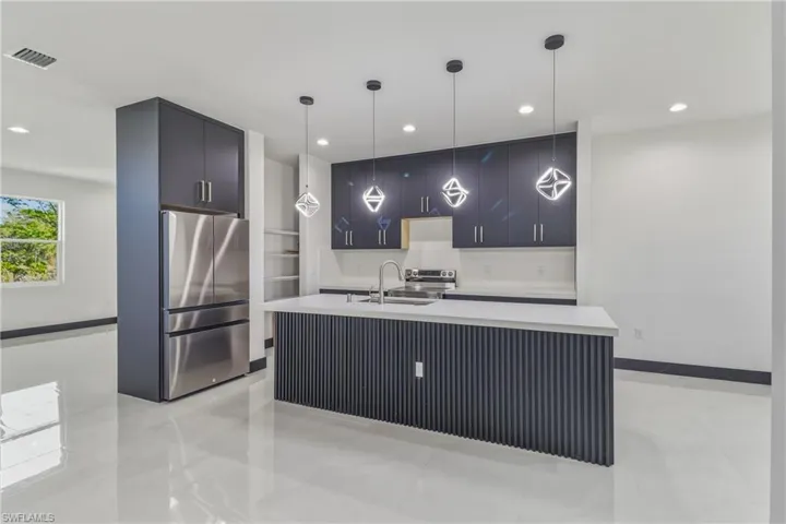 Kitchen featuring stainless steel appliances, modern cabinets, decorative light fixtures, a kitchen island with sink, and light stone counters
