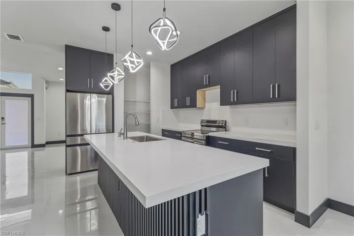 Kitchen with stainless steel appliances, dark cabinets, a center island with sink, modern cabinets, and pendant lighting