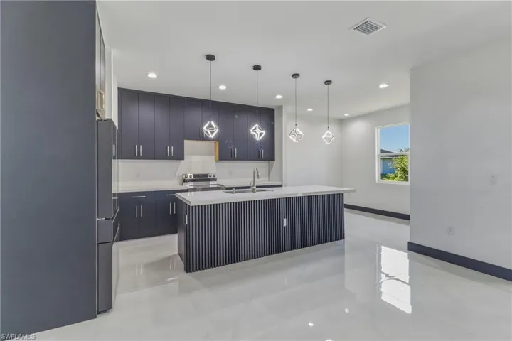 Kitchen with modern cabinets, a kitchen island with sink, freestanding refrigerator, hanging light fixtures, and electric stove