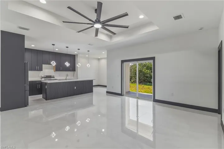 Kitchen with a center island with sink, light countertops, a tray ceiling, pendant lighting, and open floor plan