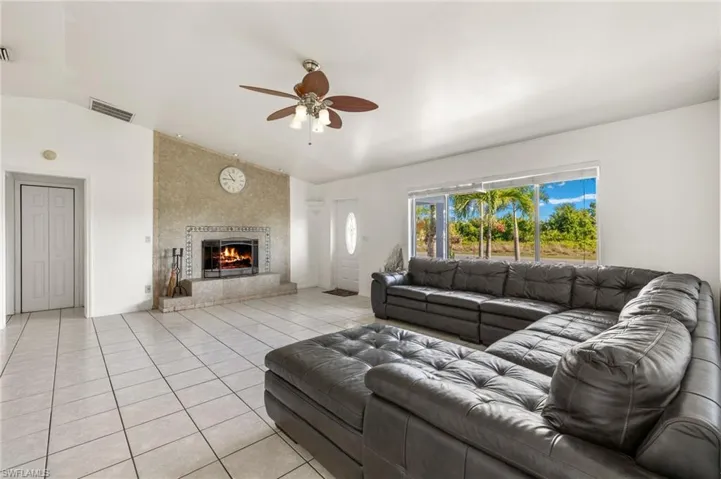 Living room featuring ceiling fan, vaulted ceiling, a large fireplace, and light tile floors