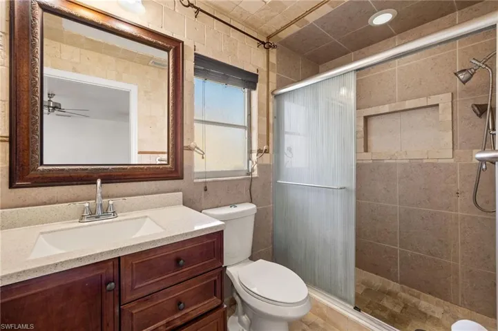 Bathroom featuring an enclosed shower, vanity, toilet, and ceiling fan