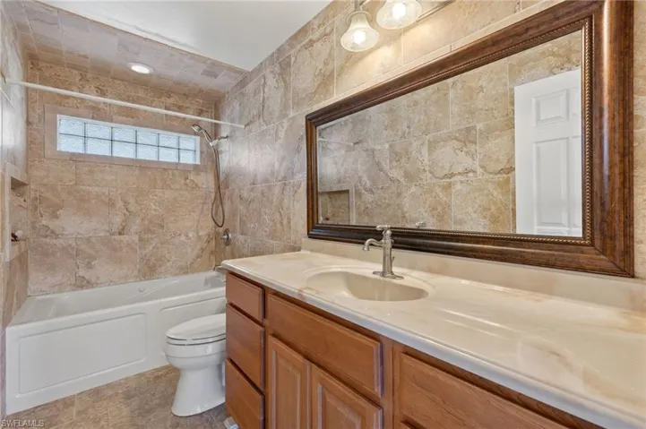 Full bathroom with tile walls, toilet, tile floors, tiled shower / bath combo, and vanity