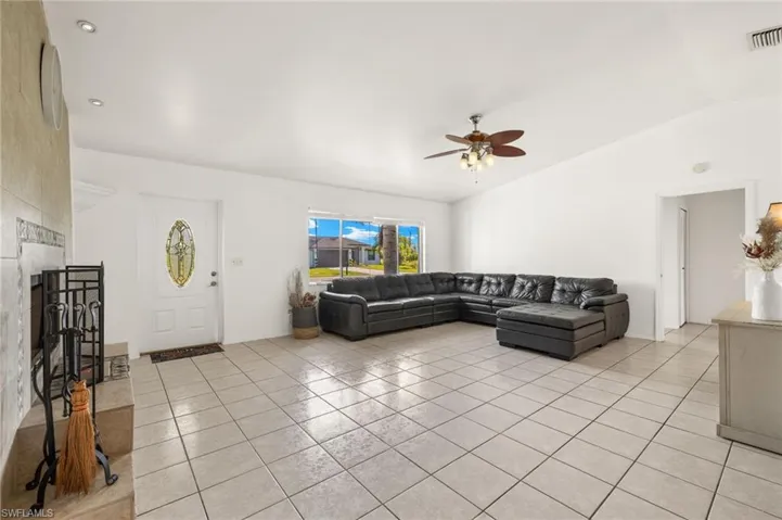 Living room with vaulted ceiling, ceiling fan, and light tile floors