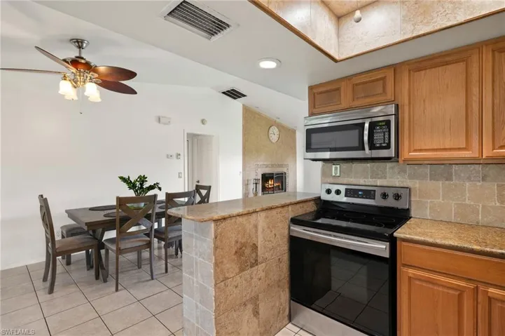 Kitchen featuring a fireplace, stainless steel appliances, light tile flooring, ceiling fan, and vaulted ceiling