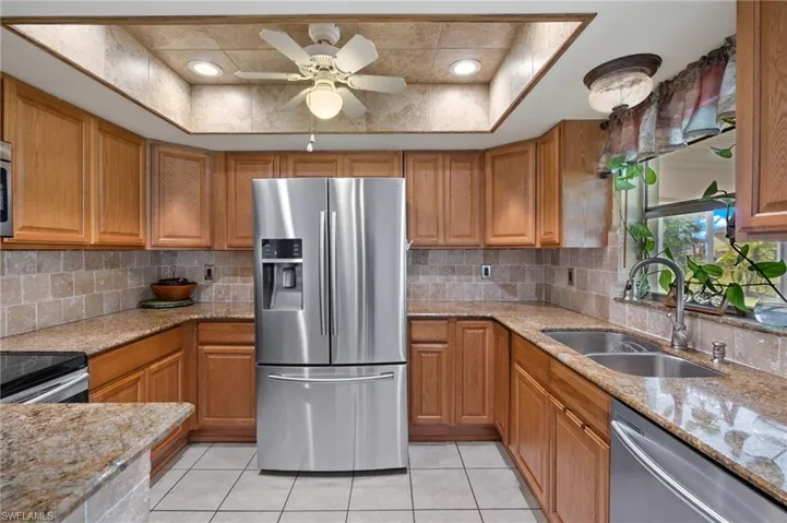 Kitchen with stainless steel appliances, sink, tasteful backsplash, ceiling fan, and a raised ceiling