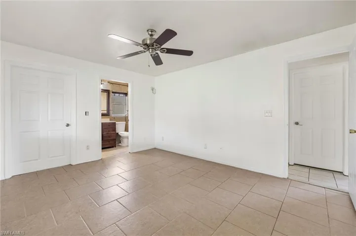 Unfurnished bedroom with connected bathroom, ceiling fan, and light tile floors