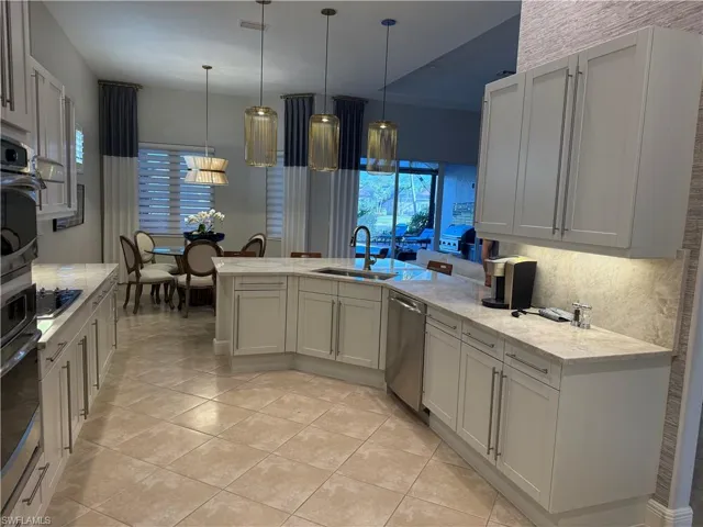Kitchen with decorative light fixtures, a peninsula, light stone countertops, dishwasher, and white cabinets