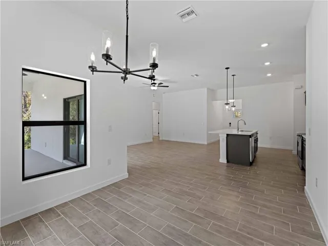 Unfurnished living room featuring light wood-type flooring, ceiling fan with notable chandelier, and sink