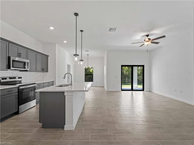 Kitchen with gray cabinetry, sink, an island with sink, and stainless steel appliances