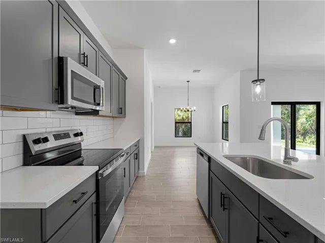 Kitchen with stainless steel appliances, sink, light stone counters, decorative light fixtures, and gray cabinets