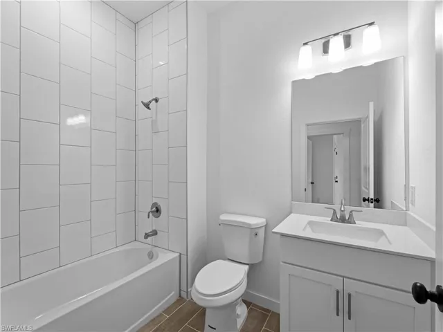 Full bathroom with vanity, tiled shower / bath combo, toilet, and wood-type flooring