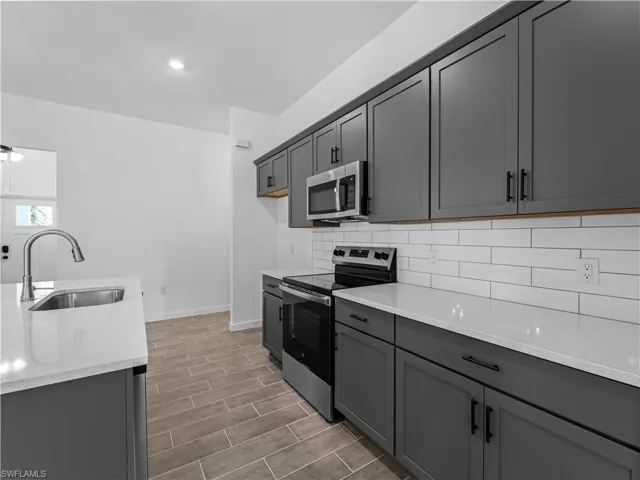 Kitchen featuring stainless steel appliances, sink, light stone counters, dark hardwood / wood-style floors, and gray cabinetry