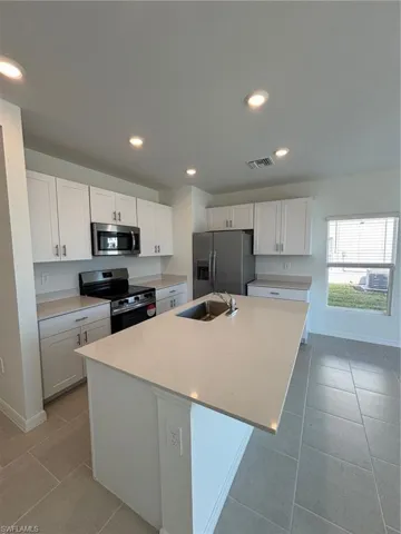 Kitchen with stove, white cabinets, stainless steel refrigerator with ice dispenser, recessed lighting, and an island with sink