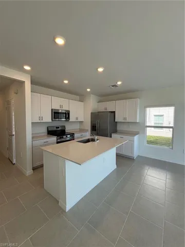 Kitchen featuring stove, white cabinetry, stainless steel refrigerator with ice dispenser, an island with sink, and recessed lighting