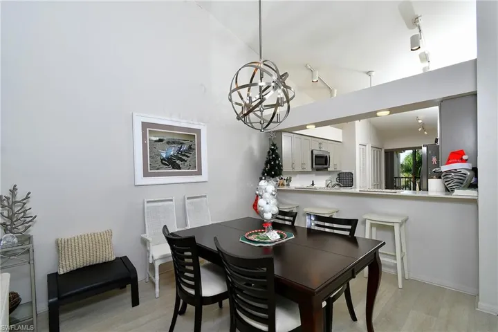 Dining room with rail lighting, light wood-type flooring, a chandelier, and vaulted ceiling