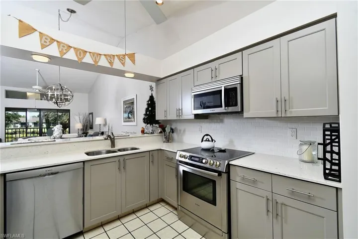 Kitchen featuring gray cabinetry, stainless steel appliances, light stone countertops, backsplash, and vaulted ceiling