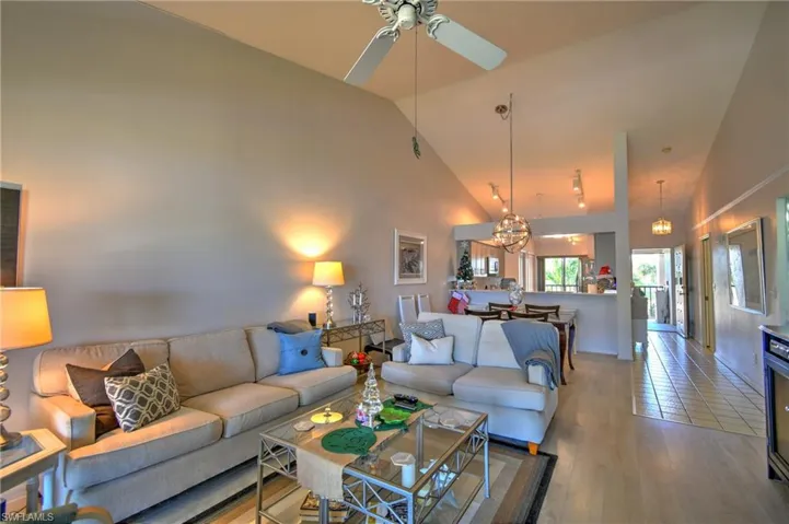 Living area with high vaulted ceiling, wood finished floors, a chandelier, and a ceiling fan