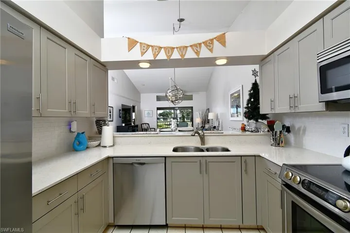 Kitchen with decorative backsplash, gray cabinets, vaulted ceiling, appliances with stainless steel finishes, and a chandelier