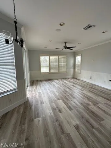 Unfurnished living room featuring wainscoting, ornamental molding, wood finished floors, a ceiling fan, and hanging lights