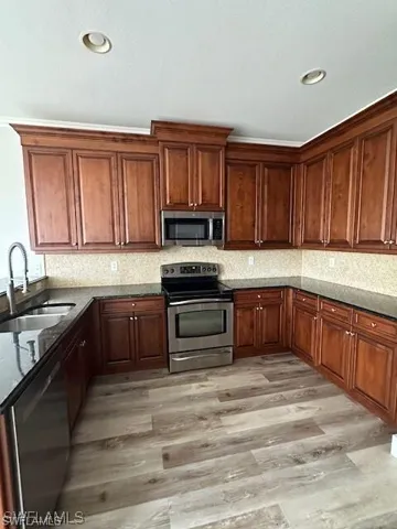 Kitchen with stainless steel appliances, dark stone countertops, light wood-style flooring, backsplash, and recessed lighting