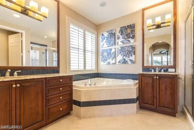 Master Bathroom featuring a stall shower, two vanities, a roman  tub, and light tile patterned flooring