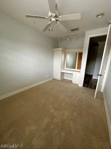 Unfurnished bedroom featuring built in study area, rail lighting, ceiling fan, and carpet floors. Can be used as a Home office