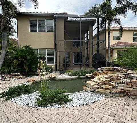 Rear view of property featuring a sunroom, a patio area, stucco siding, glass enclosure, and a garden pond