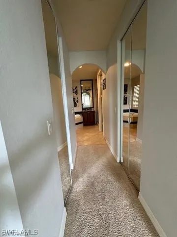 Hall featuring arched walkways, a textured wall, and light colored carpet