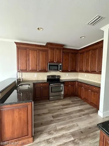 Kitchen featuring dark stone counters, stainless steel appliances, backsplash, a peninsula, and crown molding