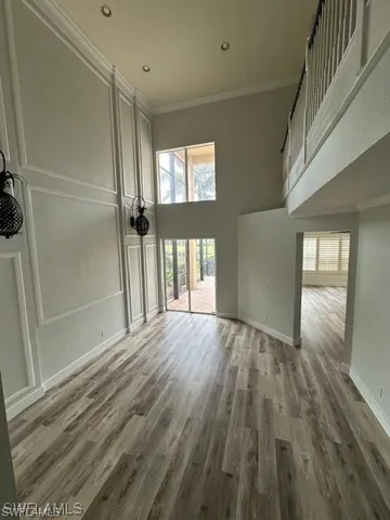 Unfurnished living room featuring a high ceiling, crown molding, light wood-style flooring, a decorative wall, and recessed lighting